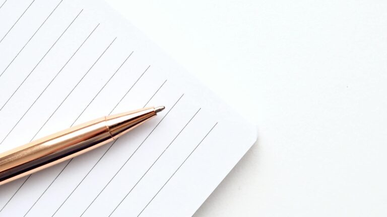 A close-up shot of a gold pen on a lined notepad with a white background, offering ample copyspace.