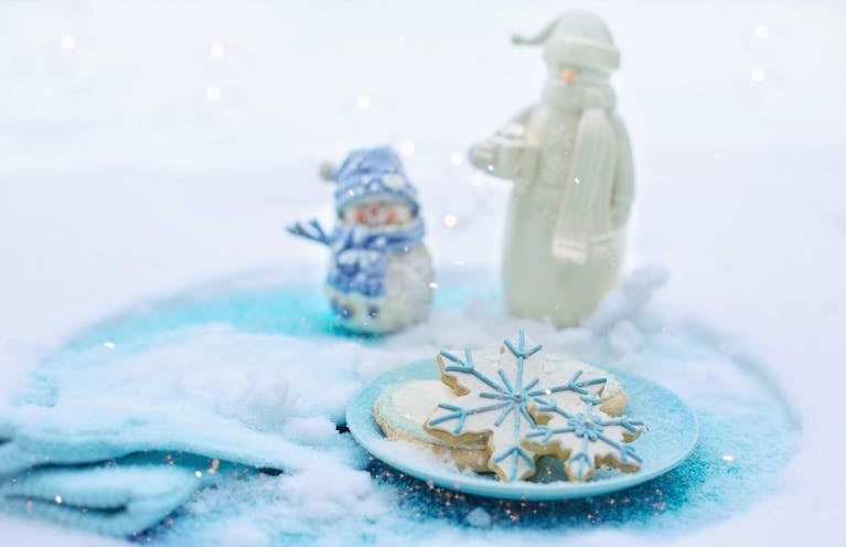 Delightful snowflake cookies on a snowy plate with snowmen figurines in a wintery scene.