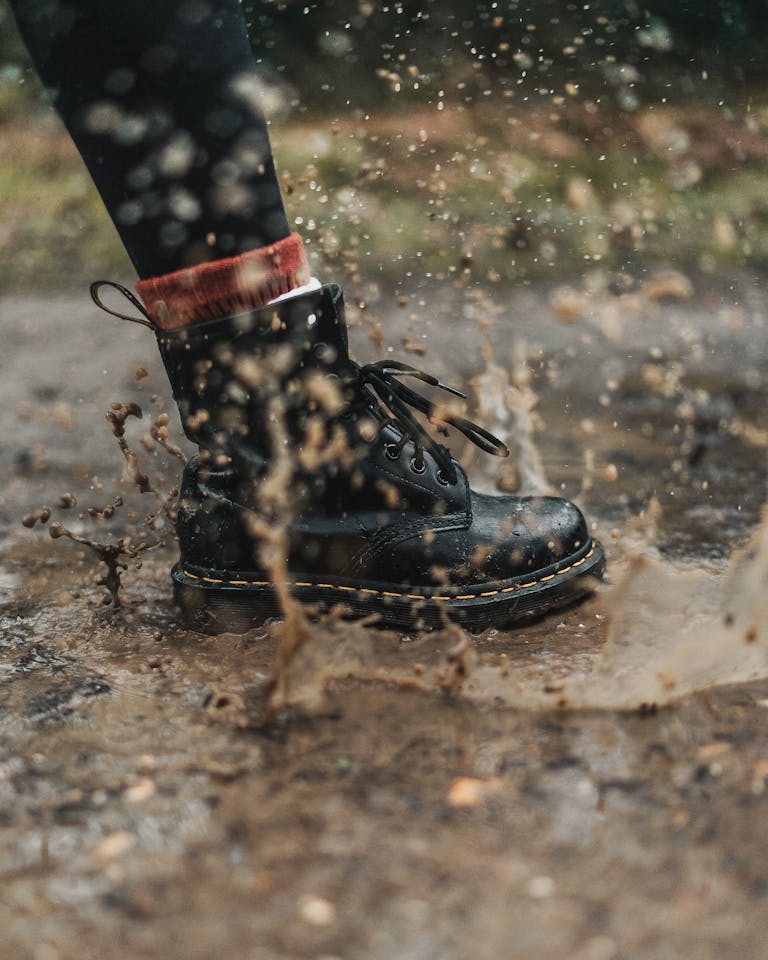 A black boot splashes through a muddy puddle, capturing the essence of rainy weather.